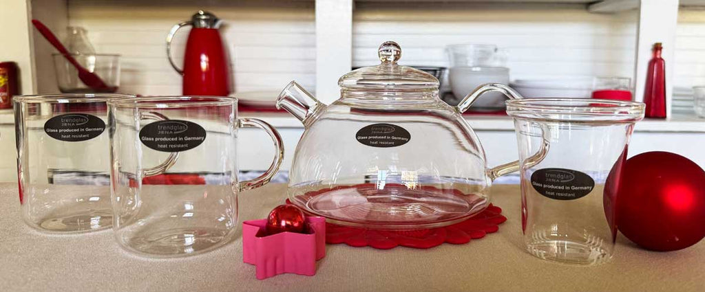 Clear glass mugs and teapot with red ornaments on a kitchen counter